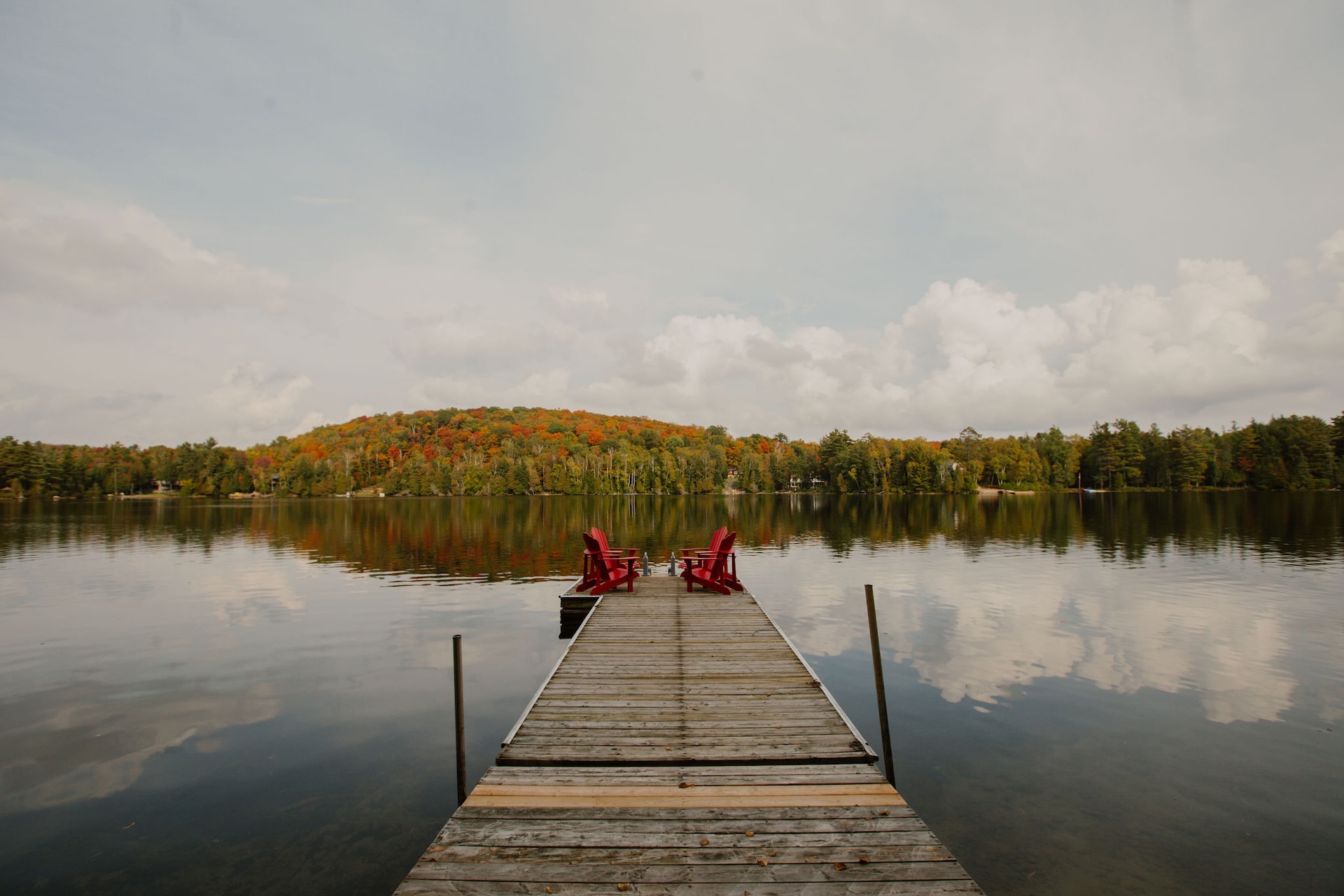Dock with red Adirondack chairs and fall foliage lake view